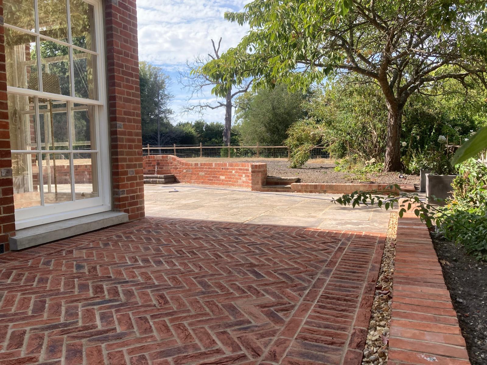 Completed brick paved patio beside a house and garden