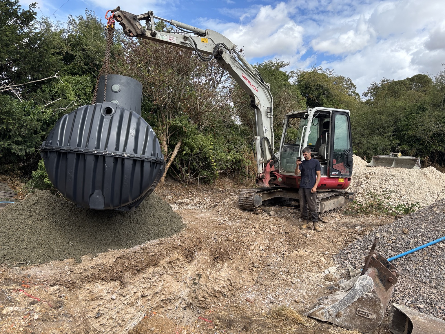Excavator lifting a wastewater tank into position on site
